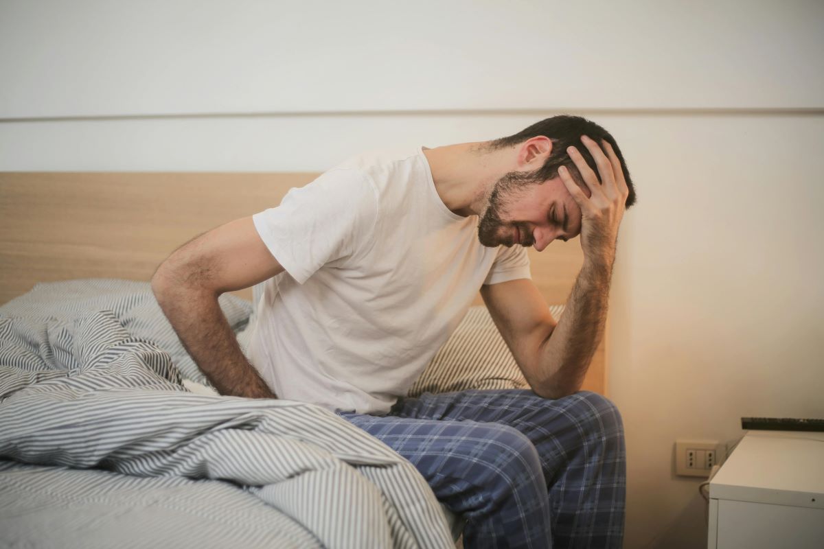 Bărbat cu migrenă care stă la marginea patului cu mâna pe frunte